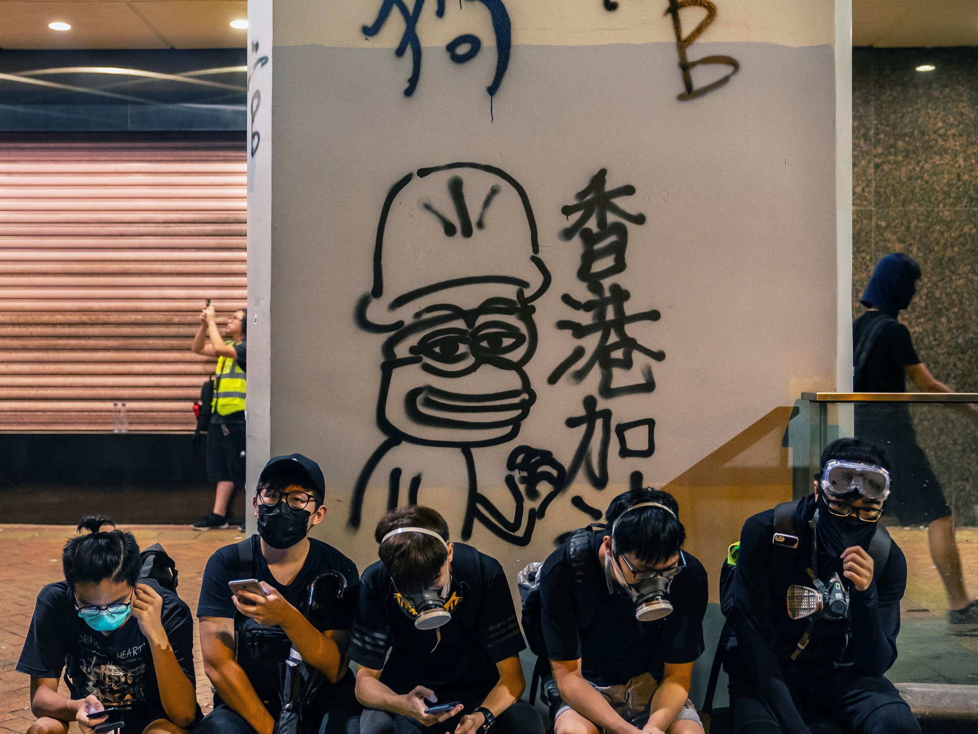 HK protestors sit in front of Pepe graffiti.